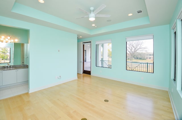 tiled empty room featuring ceiling fan, a tray ceiling, and sink