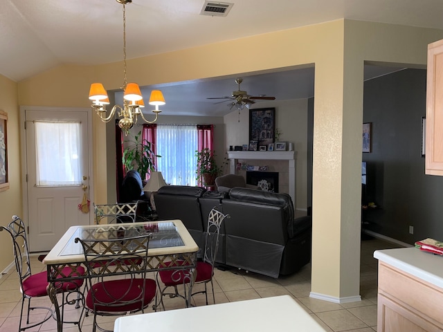 dining space featuring light tile floors, a tile fireplace, ceiling fan with notable chandelier, and vaulted ceiling