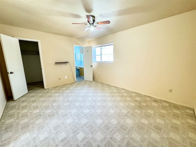 unfurnished bedroom featuring a walk in closet, light colored carpet, ceiling fan, and ensuite bath