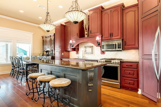 kitchen with a kitchen island, hanging light fixtures, appliances with stainless steel finishes, dark wood-type flooring, and tasteful backsplash