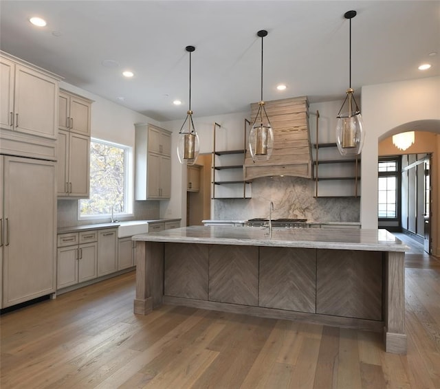 kitchen with paneled refrigerator, pendant lighting, an island with sink, and light hardwood / wood-style flooring