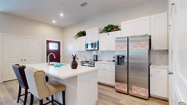 kitchen featuring appliances with stainless steel finishes, light wood-type flooring, tasteful backsplash, and an island with sink