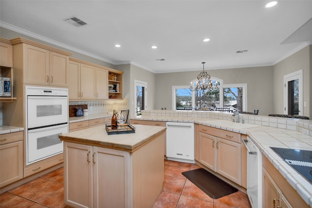 kitchen with a kitchen island, white appliances, decorative backsplash, tile counters, and a chandelier