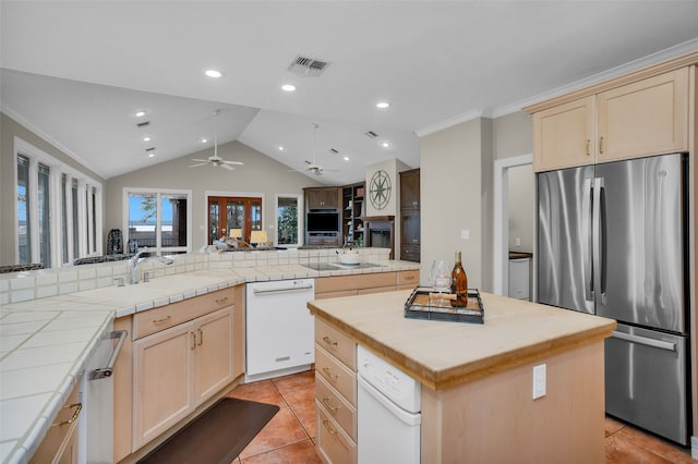 kitchen with stainless steel refrigerator, light brown cabinets, vaulted ceiling, kitchen peninsula, and a center island