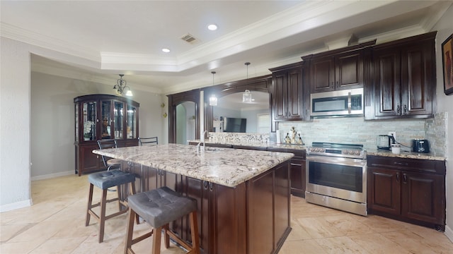 kitchen with decorative light fixtures, a kitchen bar, appliances with stainless steel finishes, backsplash, and a tray ceiling