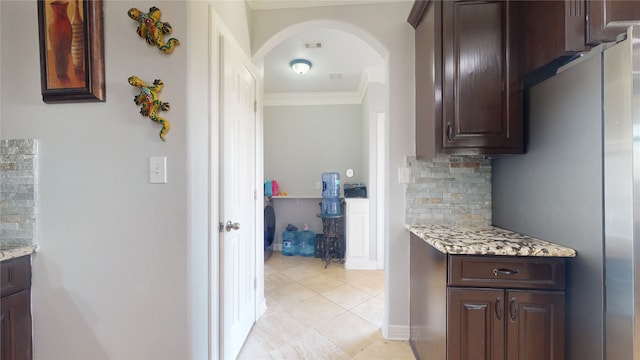 kitchen featuring light tile floors, ornamental molding, light stone countertops, tasteful backsplash, and dark brown cabinetry