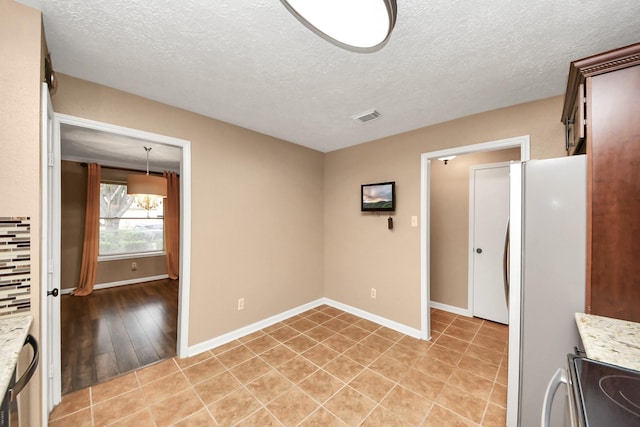 kitchen featuring stove, light tile patterned floors, a textured ceiling, and white refrigerator