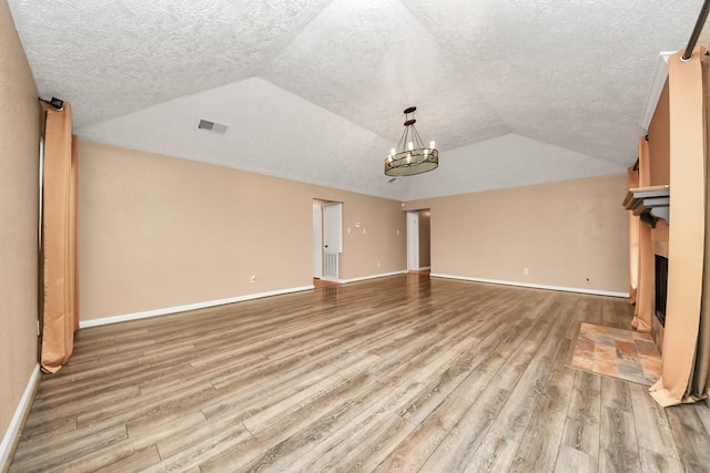 unfurnished living room with light hardwood / wood-style floors, lofted ceiling, a textured ceiling, and a tiled fireplace