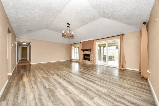 unfurnished living room featuring a fireplace, a chandelier, vaulted ceiling, and light hardwood / wood-style flooring