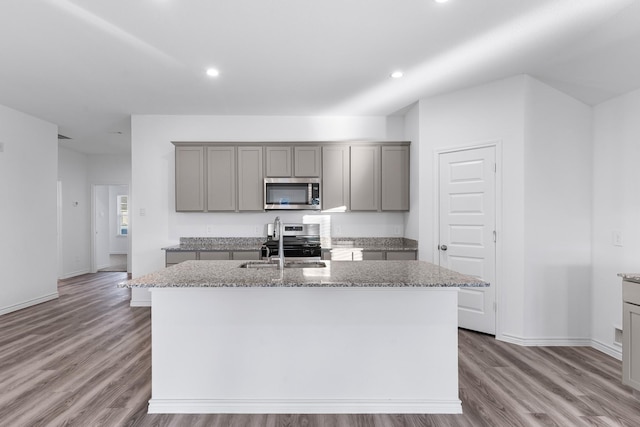 kitchen with light stone countertops, sink, gray cabinets, a center island with sink, and appliances with stainless steel finishes