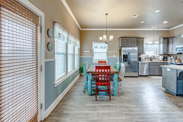 dining area with a chandelier, crown molding, sink, and light wood-type flooring