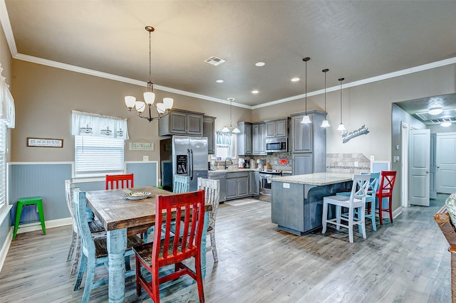 dining area featuring light hardwood / wood-style flooring, ornamental molding, a notable chandelier, and a wealth of natural light