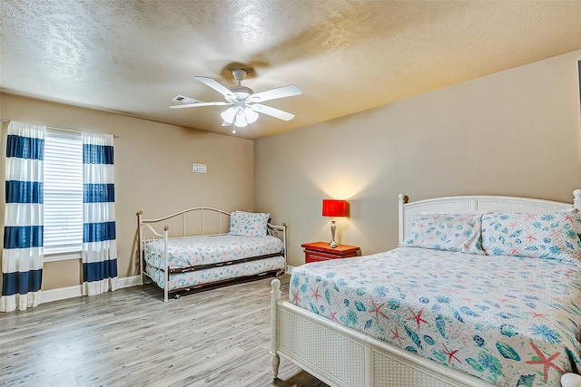 bedroom with a textured ceiling, ceiling fan, and light hardwood / wood-style flooring