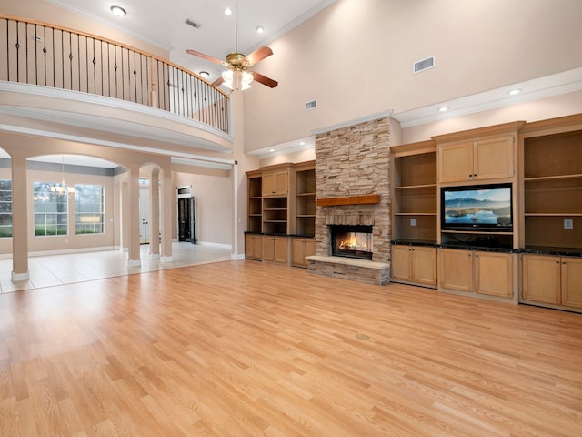 unfurnished living room featuring light tile floors, ceiling fan, a towering ceiling, and a fireplace