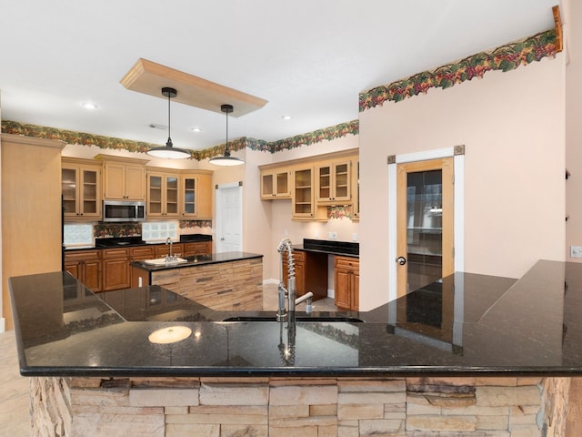 kitchen featuring tasteful backsplash, dark stone countertops, decorative light fixtures, sink, and kitchen peninsula