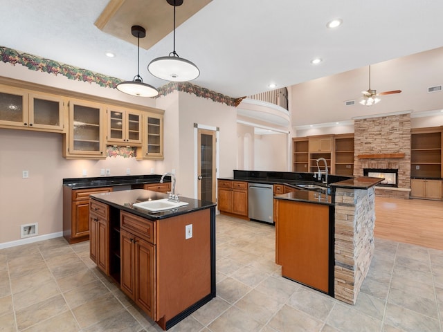 kitchen featuring a stone fireplace, a center island with sink, stainless steel dishwasher, pendant lighting, and ceiling fan