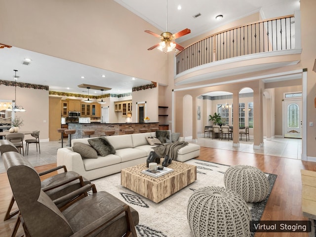 living room with crown molding, ceiling fan with notable chandelier, light tile floors, and a high ceiling