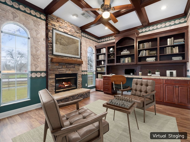 living area with coffered ceiling, beamed ceiling, ceiling fan, light hardwood / wood-style flooring, and a fireplace