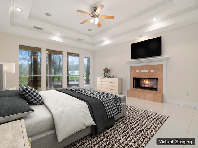 bedroom with a tiled fireplace, ceiling fan, light tile flooring, and a tray ceiling