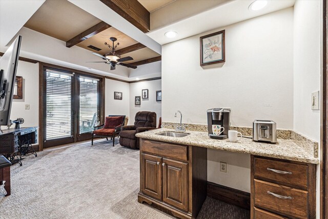 office space featuring light colored carpet, ceiling fan, sink, built in desk, and beamed ceiling