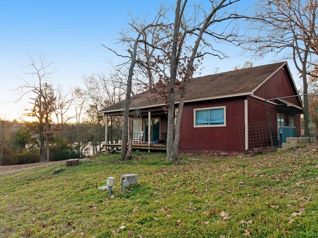 back house at dusk featuring a porch and a lawn