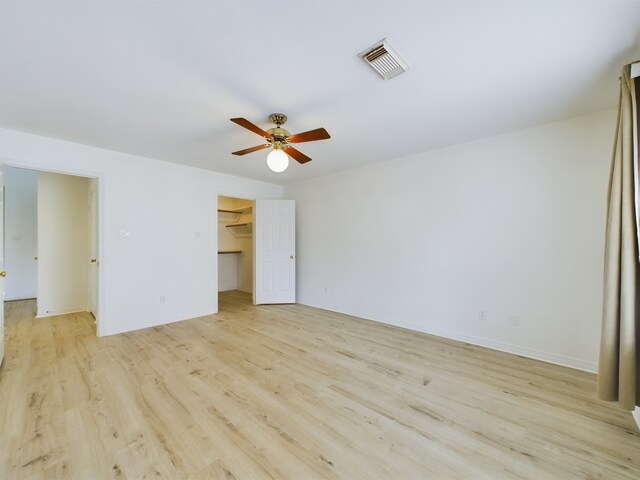 unfurnished bedroom featuring a closet, light hardwood / wood-style floors, a spacious closet, and ceiling fan