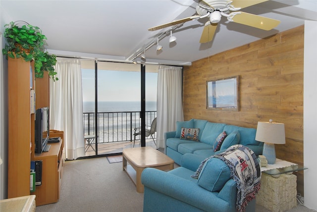 carpeted living room with wooden walls, a water view, ceiling fan, and track lighting