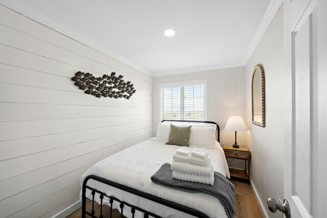 bedroom featuring ornamental molding, wood-type flooring, and wood walls