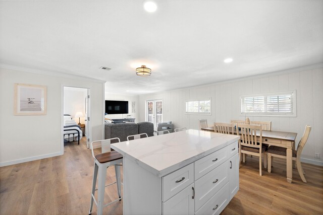 kitchen with a breakfast bar, crown molding, light hardwood / wood-style flooring, a kitchen island, and white cabinets