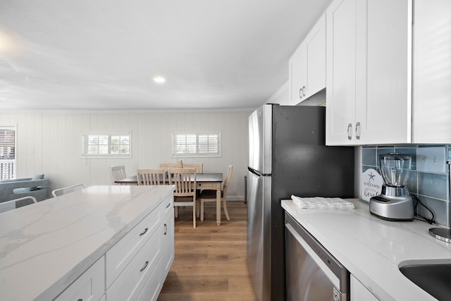 kitchen with stainless steel appliances, white cabinetry, light stone countertops, and wood-type flooring