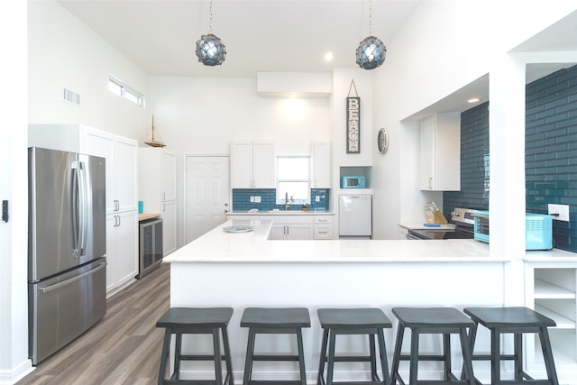 kitchen with white cabinets, appliances with stainless steel finishes, dark hardwood / wood-style floors, kitchen peninsula, and tasteful backsplash