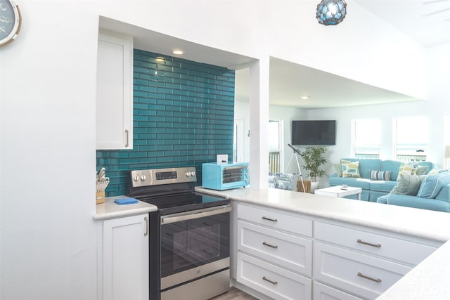 kitchen with stainless steel electric range, tasteful backsplash, and white cabinets