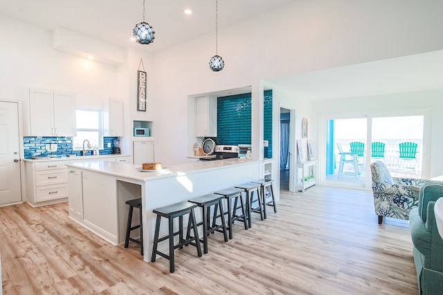 kitchen featuring white cabinets, hanging light fixtures, light hardwood / wood-style floors, a kitchen breakfast bar, and high vaulted ceiling