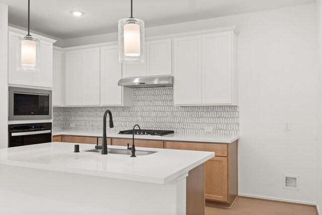 kitchen featuring white cabinets, pendant lighting, appliances with stainless steel finishes, light hardwood / wood-style flooring, and backsplash