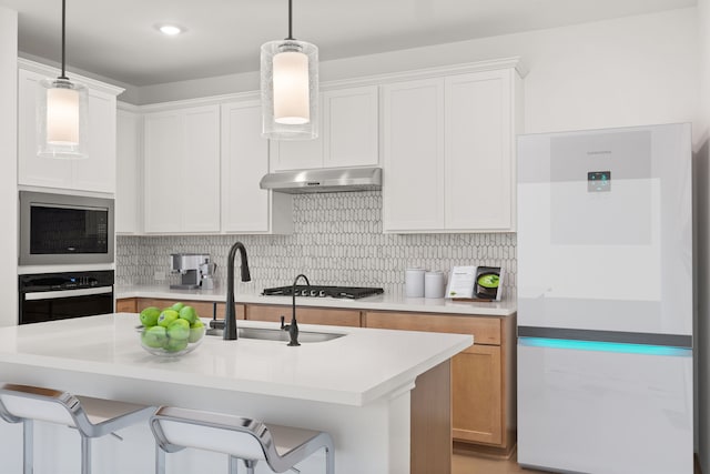 kitchen with appliances with stainless steel finishes, decorative backsplash, white cabinets, and a center island with sink