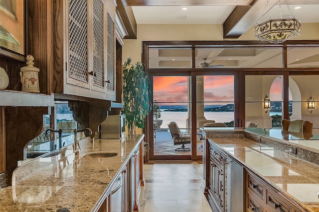 kitchen featuring coffered ceiling, pendant lighting, a water view, light stone counters, and sink