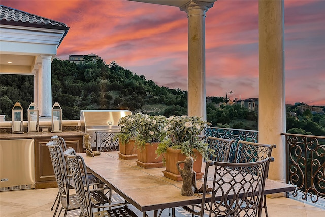 patio terrace at dusk with a grill, a balcony, and exterior kitchen