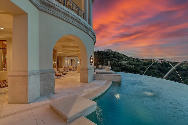 pool at dusk with a patio area and pool water feature