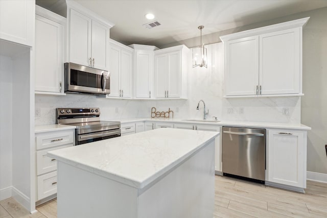 kitchen with appliances with stainless steel finishes, decorative light fixtures, white cabinetry, and sink