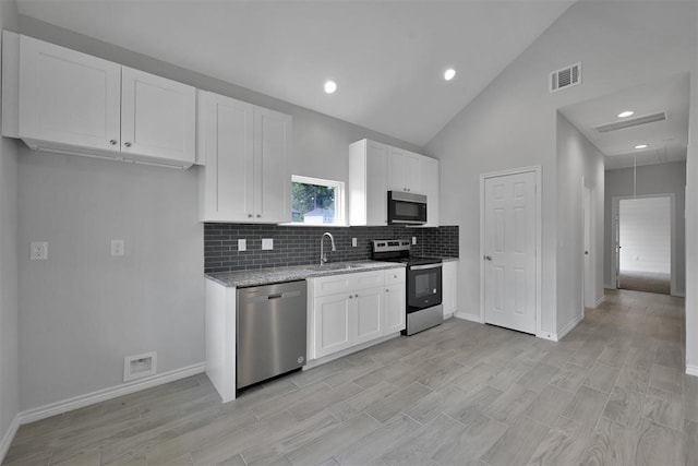 kitchen with light wood-type flooring, stainless steel appliances, sink, light stone countertops, and white cabinets