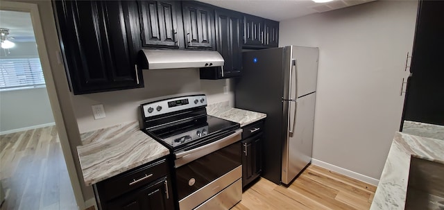 kitchen featuring appliances with stainless steel finishes, light wood-style floors, light stone countertops, under cabinet range hood, and baseboards