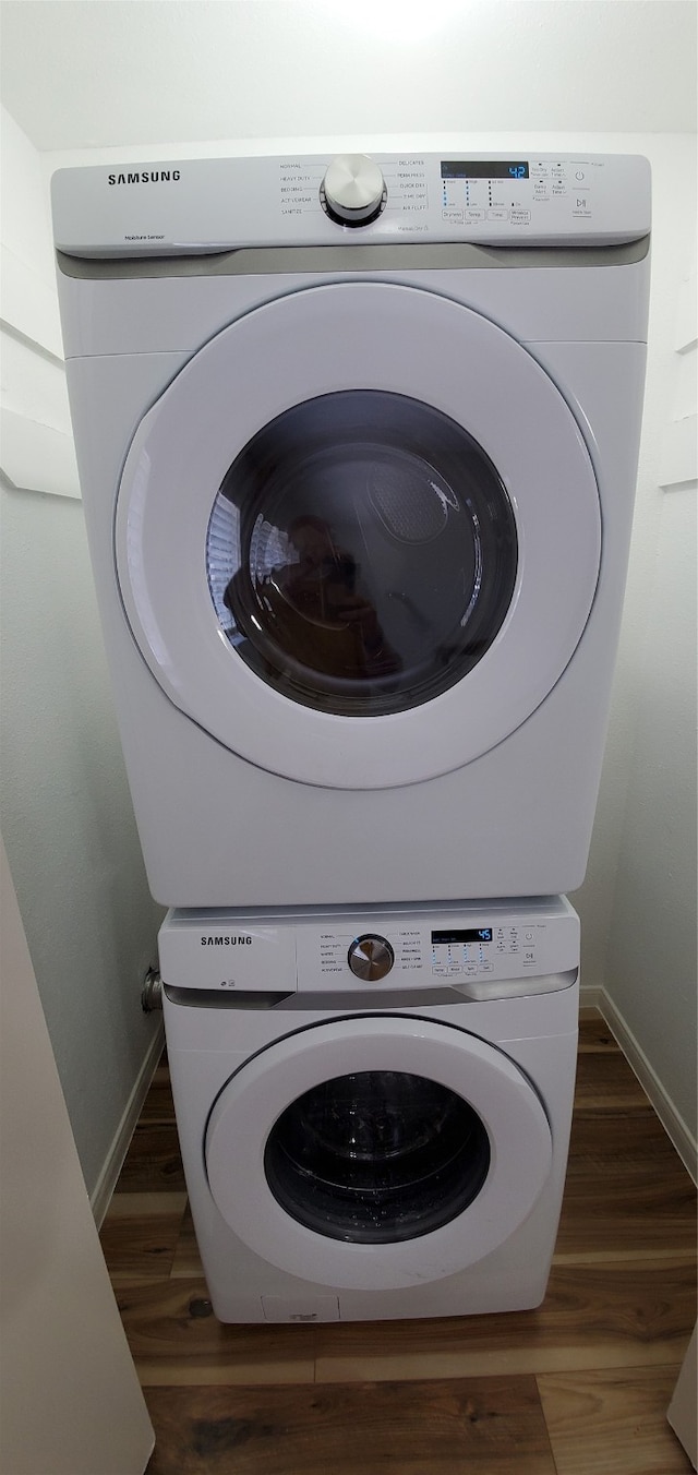 clothes washing area with laundry area, baseboards, dark wood-style flooring, and stacked washer / dryer