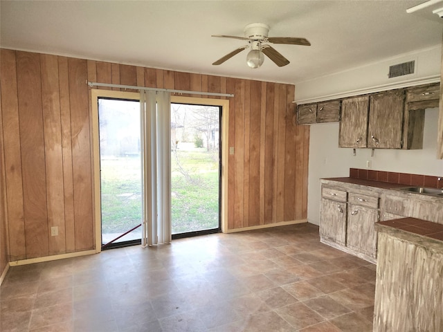 kitchen featuring ceiling fan, wooden walls, tile flooring, and sink