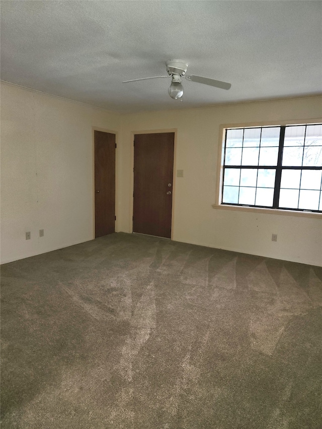 spare room with a textured ceiling, ceiling fan, and dark colored carpet