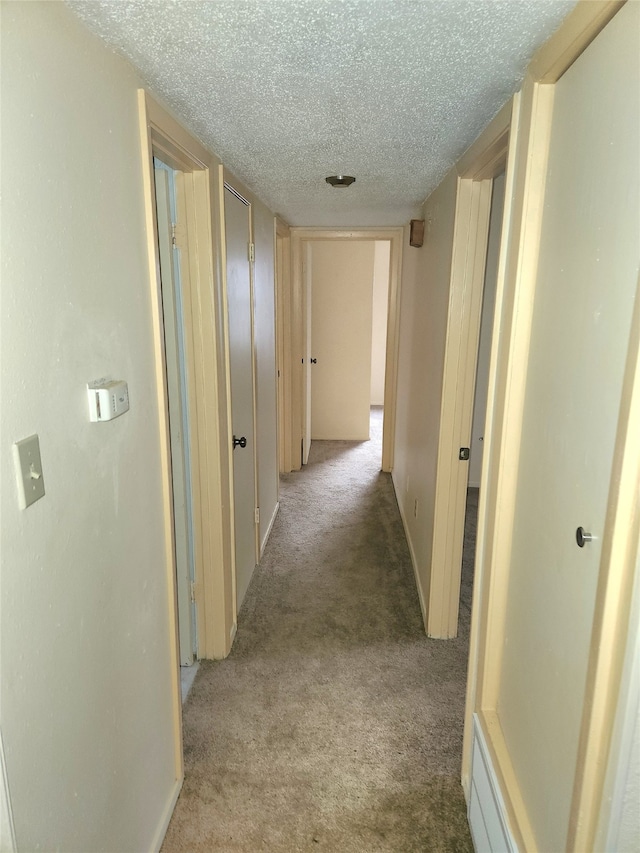 corridor with light colored carpet and a textured ceiling