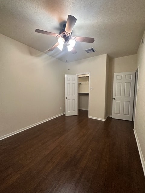 unfurnished bedroom with ceiling fan, dark hardwood / wood-style floors, a spacious closet, and a textured ceiling