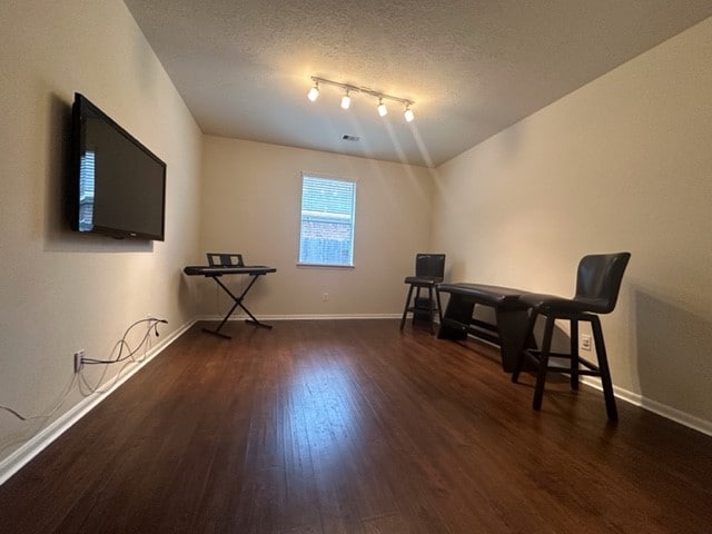 interior space featuring a textured ceiling, rail lighting, and dark hardwood / wood-style flooring