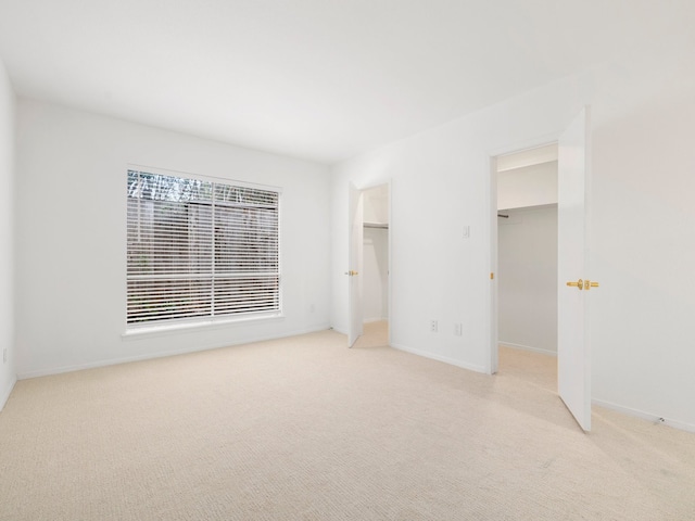 unfurnished bedroom featuring light colored carpet, a walk in closet, and a closet