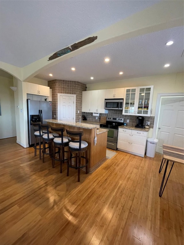 239 Heron St Unit Cr299, Sargent, TX 77414 - kitchen featuring appliances with stainless steel finishes, backsplash, a kitchen breakfast bar, arched walkways, and glass insert cabinets