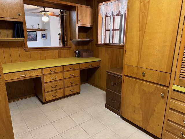 kitchen with light tile patterned flooring, wood walls, ceiling fan, and built in desk